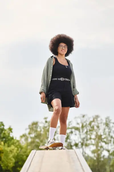 A young African American woman with an afro is skateboarding gracefully on a ramp in an outdoor skate park. — Stock Photo