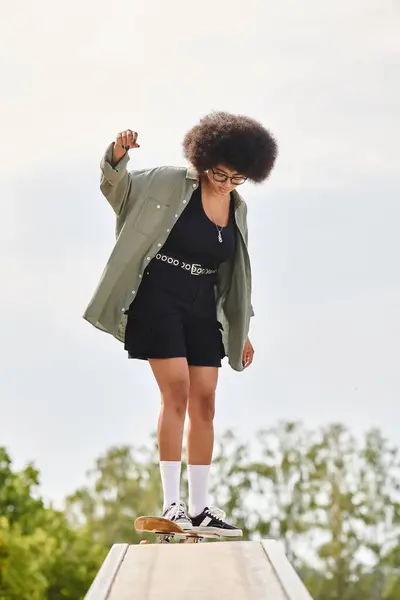 Uma mulher afro-americana com cabelo encaracolado monta um skate em uma rampa de madeira em um parque de skate. — Fotografia de Stock