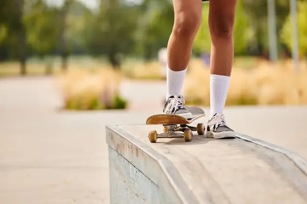 Una joven afroamericana patinando en una cornisa en un parque de skate al aire libre. - foto de stock