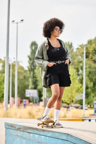 Young woman with curly hair rides skateboard on top of ramp in urban skate park. — Stock Photo