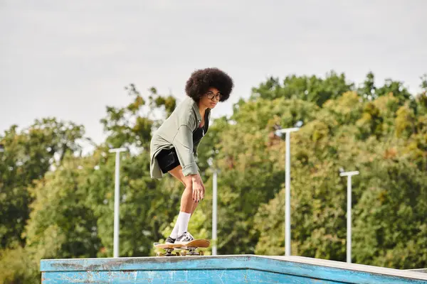 Une jeune afro-américaine aux cheveux bouclés monte gracieusement sa planche à roulettes sur une rampe dans un skate park en plein air. — Photo de stock