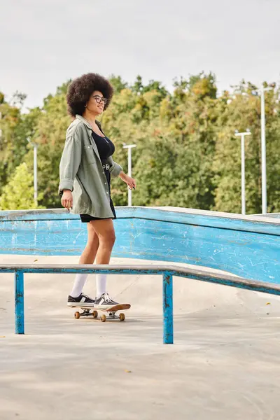Young African American woman with curly hair rides a skateboard fearlessly on a metal rail at an outdoor skate park. — Stock Photo