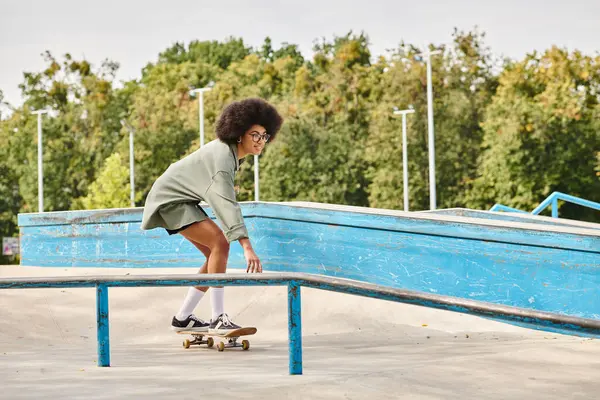 A young African American woman with curly hair skillfully rides a skateboard on a rail in an outdoor skate park. — Stock Photo