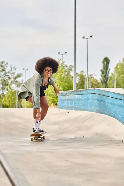 A young African American woman with curly hair gracefully skateboards down a ramp at an outdoor skate park. — Stock Photo
