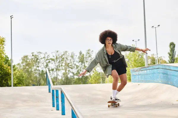 A young African American woman with curly hair confidently rides a skateboard down the side of a ramp at an outdoor skate park. — Stock Photo