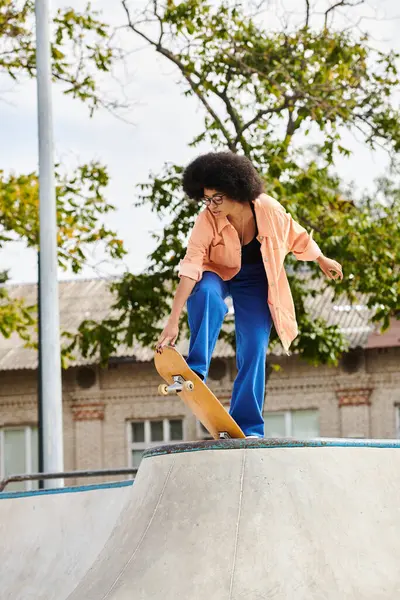 A young African American woman with curly hair skillfully skateboarding on a ramp at an outdoor skate park. — Stock Photo