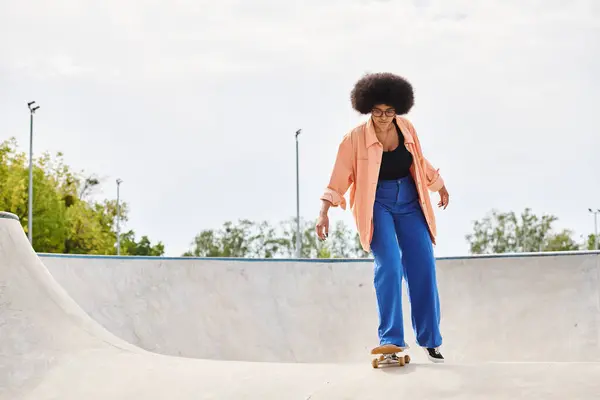 A young African American woman with curly hair skilfully rides a skateboard up the side of a ramp in a vibrant skate park. — Stock Photo