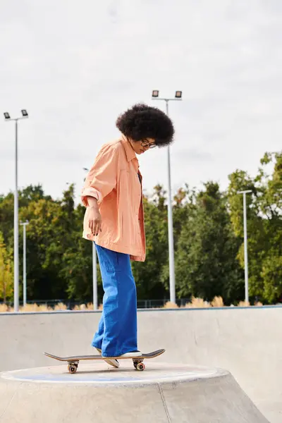 Une jeune Afro-Américaine avec des cheveux bouclés skateboard sur une rampe dans un parc de skate en plein air dynamique. — Photo de stock