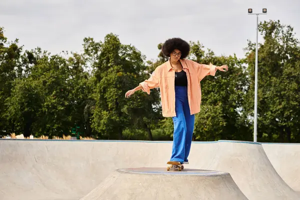 A young African American woman with curly hair confidently rides her skateboard up the side of a ramp at a skate park. — Stock Photo