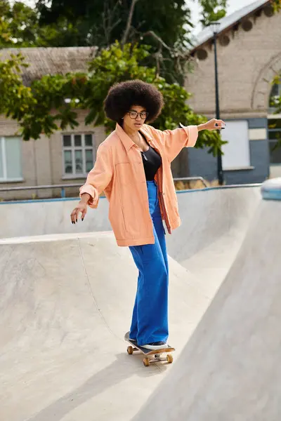 Une jeune afro-américaine aux cheveux bouclés monte en toute confiance une planche à roulettes sur le côté d'une rampe dans un skate park en plein air. — Photo de stock