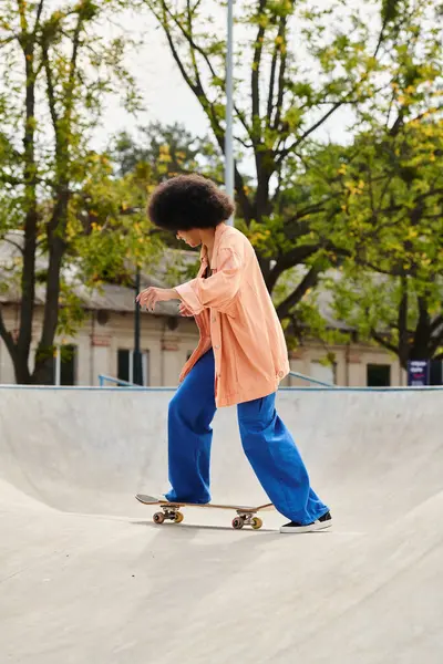 A young African American woman with curly hair glides down a ramp on a skateboard in an outdoor skate park. — Stock Photo