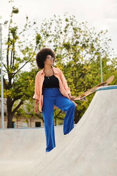 Jeune femme afro-américaine aux cheveux bouclés skateboard en toute confiance dans un parc de skate dynamique. — Photo de stock