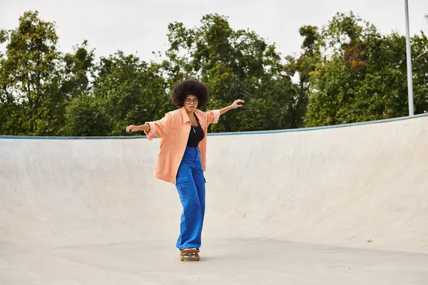 Une jeune Afro-Américaine aux cheveux bouclés monte énergiquement une planche à roulettes sur une rampe dans un skate park urbain. — Photo de stock