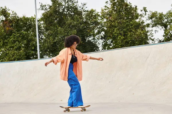 Eine junge Afroamerikanerin mit lockigem Haar fährt in einem Outdoor-Skatepark gekonnt mit einem Skateboard die Seite einer Rampe hinauf. — Stockfoto