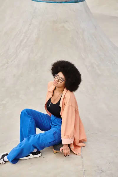 Mulher afro-americana nova elegante com cabelo encaracolado senta-se em um skate em um parque de skate urbano vibrante. — Fotografia de Stock