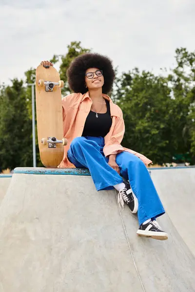 Молода афроамериканка з кучерявим волоссям сидить на скейтборді. Вона висловлює впевненість і рішучість. — стокове фото