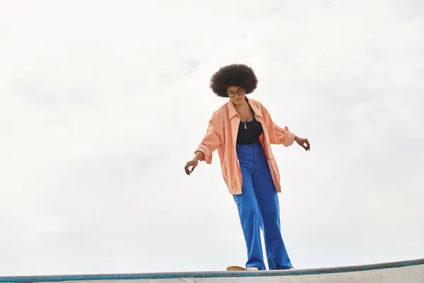 A young African American woman with curly hair confidently stands on a skateboard on a ramp, showcasing her skateboarding skills. — Stock Photo