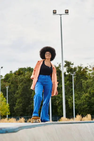 An African American woman with curly hair skateboarding on top of a ramp at an outdoor skate park. — Stock Photo
