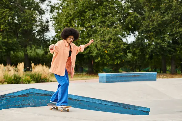 A young African American woman with curly hair fearlessly rides a skateboard on top of a ramp in a vibrant skate park. — Stock Photo