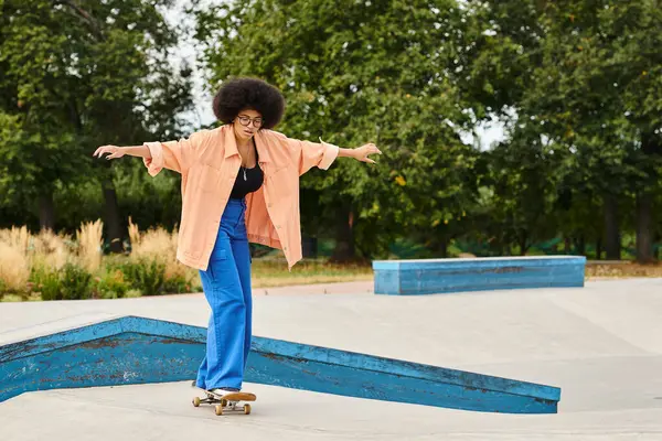 A young African American woman with curly hair rides a skateboard confidently on top of a ramp at an outdoor skate park. — Stock Photo