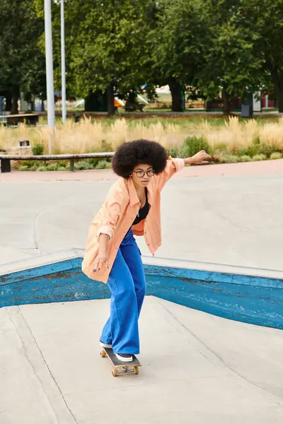 Young African American woman with curly hair rides skateboard down cement ramp at outdoor skate park. — Stock Photo