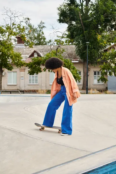 Mujer negra hábilmente monta un monopatín en la parte superior de una rampa de cemento en un parque de skate al aire libre. - foto de stock
