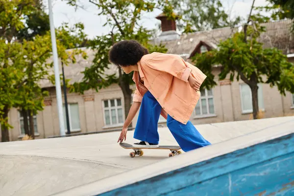 Молода афроамериканка з кучерявим скейтбордингом на пандусі у відкритому скейт-парку. — стокове фото