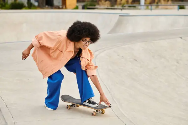 Una giovane donna afroamericana con lo skateboard dei capelli ricci in un vivace skate park, mostrando abilità sullo skateboard. — Foto stock