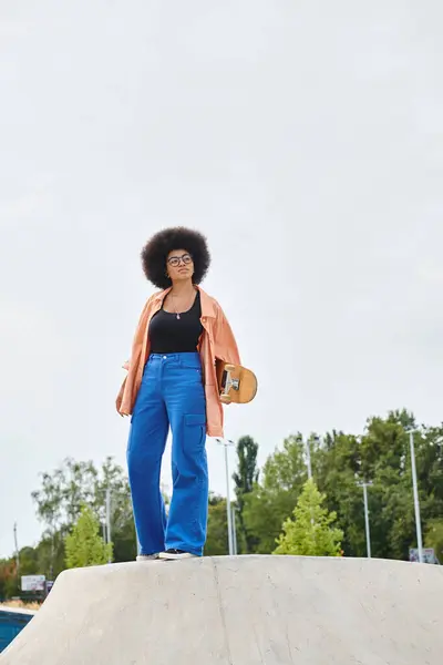 A young African American woman stands confidently on top of a skateboard ramp at an outdoor skate park. — Stock Photo