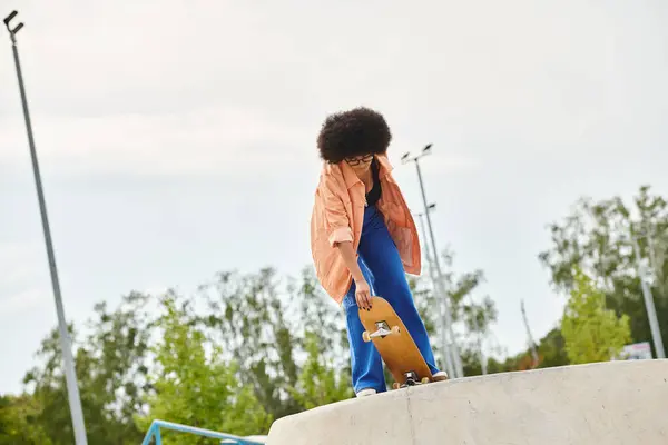 Une jeune femme aux cheveux bouclés, pleine d'énergie audacieuse, monte son skateboard sur le côté escarpé d'une rampe dans un affichage dynamique d'habileté et d'agilité. — Photo de stock