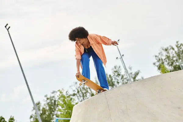 Athlète jeune femme afro-américaine habilement monte une planche à roulettes sur une rampe raide à un skate park. — Photo de stock