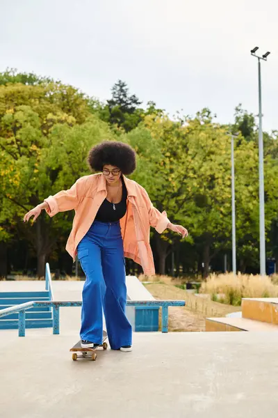 African American woman with curly hair confidently skateboarding on top of a cement slab at a skate park. — Stock Photo