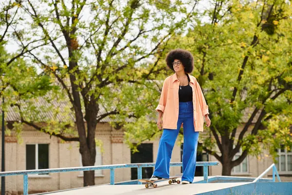 Young African American woman with curly hair skillfully riding a skateboard on top of a ramp at an outdoor skate park. — Stock Photo