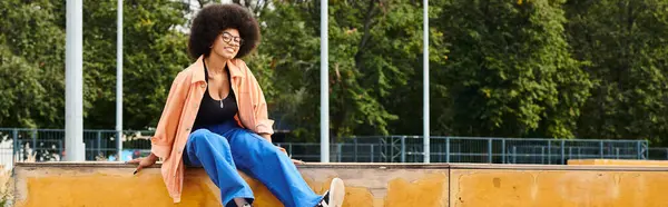 Una giovane donna afroamericana dai capelli ricci siede aggraziatamente su un muro, incrociando le gambe mentre guarda in lontananza. — Foto stock