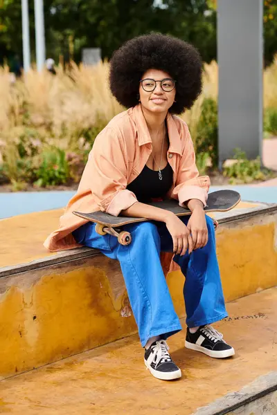 Uma jovem afro-americana com cabelo encaracolado se senta em uma borda com seu skate em um vibrante parque de skate ao ar livre. — Fotografia de Stock