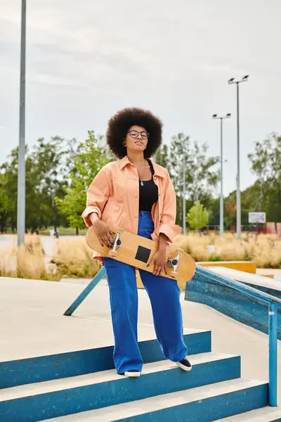 A young African American woman with curly hair confidently holds a skateboard while standing on steps outdoors. — Stock Photo