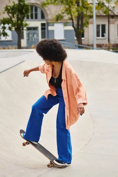 Young African American woman with curly hair skateboarding on a ramp in a vibrant outdoor skate park. — Stock Photo
