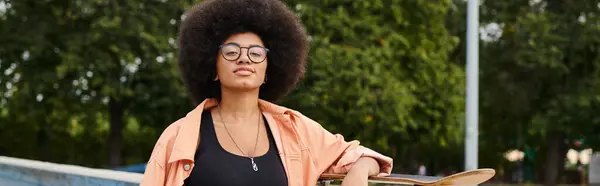 A young African American woman with an afro confidently holds a skateboard at a skate park. — Stock Photo