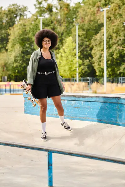 Junge Afroamerikanerin mit lockigem Haar hält ein Skateboard am schimmernden Swimmingpool. — Stockfoto