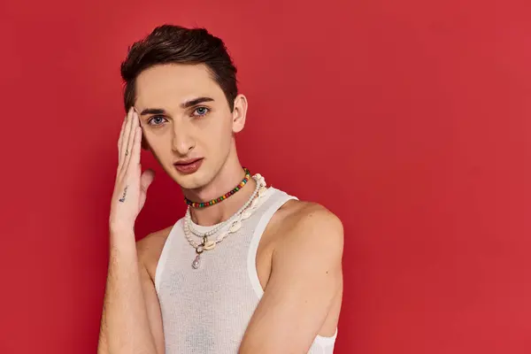 Bien parecido gay hombre en casual atuendo con accesorios en rojo fondo y mirando la cámara - foto de stock