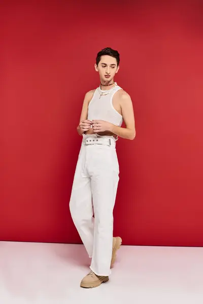 Moda atractivo gay hombre en casual atuendo con accesorios posando en rojo telón de fondo y mirando hacia otro lado - foto de stock