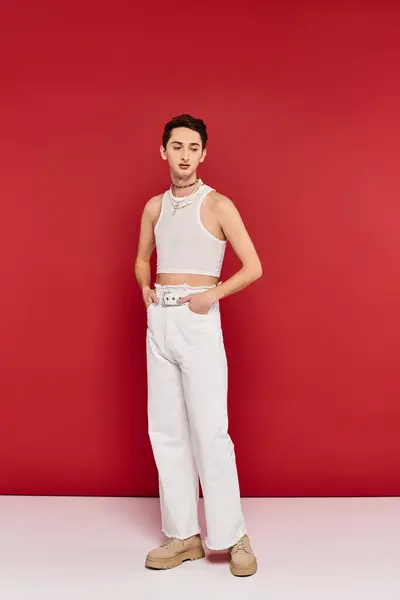 Stylish appealing gay man in casual attire with accessories posing on red backdrop and looking away — Stock Photo