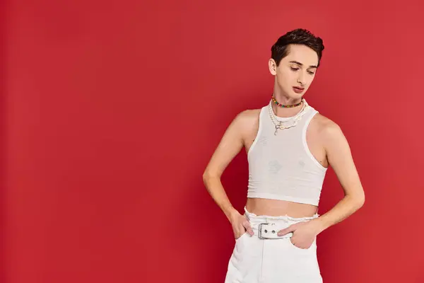 Стильный привлекательный гей в повседневной одежде с аксессуарами позируя на красном фоне и глядя в сторону — стоковое фото