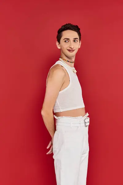 Cheerful appealing gay man in casual attire with accessories posing on red backdrop and looking away — Stock Photo