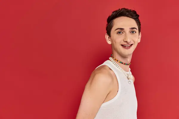 Happy handsome gay man with stylish accessories in white attire looking at camera on red backdrop — Stock Photo