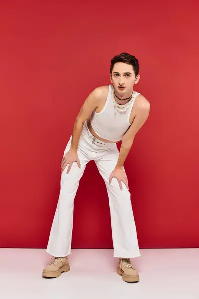 Attrayant gay l'homme en tenue décontractée avec accessoires posant sur fond rouge et regardant caméra — Photo de stock