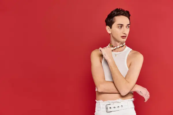 Привлекательный модный гей в повседневной одежде с аксессуарами на красном фоне и отводя взгляд — стоковое фото