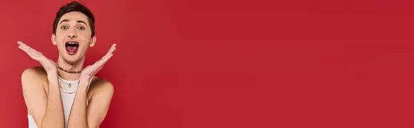 Joyful gay man with stylish accessories in white attire looking at camera on red backdrop, banner — Stock Photo