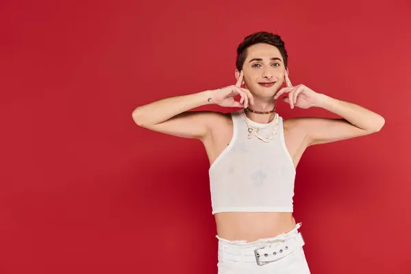 Joyous handsome gay man with stylish accessories in white attire looking at camera on red backdrop — Stock Photo