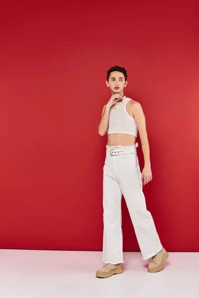 Appealing fashionable gay man in casual attire with accessories on red backdrop and looking away — Stock Photo